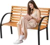 A woman sits on a wooden park bench reading a book. Anteprima dell’immagine prodotto