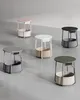Five small round tables with storage baskets underneath, arranged on a light gray floor with a textured wall behind. Produktbild-Vorschau