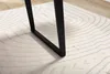 A close-up view of a black metal table leg resting on a beige rug with a wavy pattern. Voir les images du produit