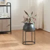 A plant in a pot on a stand next to a shelf unit. Produktbild-Vorschau
