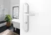 A close-up of a white door handle and lock mechanism on a white wall, with a blurred bathroom scene in the background. Produktbild-Vorschau