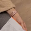 A person's wrist wearing a rose gold watch band is shown, holding an open book. Produktbild-Vorschau