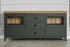 A green sideboard with a wooden top and metal legs, set against a light gray and white paneled wall. Podgląd zdjęcia produktu
