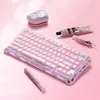A pink mechanical keyboard is displayed on a pink surface, surrounded by cosmetic items. Produktbild-Vorschau