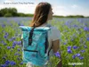 A woman wearing a backpack stands in a field of blue flowers. Produktbild-Vorschau