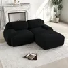 A black sectional sofa with an ottoman is placed on a light gray rug in a living room with a fireplace and a potted plant. Produktbild-Vorschau