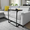 A C-shaped side table is placed next to a sectional sofa in a living room. Produktbild-Vorschau