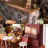 A collage of two scenes: the top shows a miniature cafe counter with tiled backsplash and wooden countertop, and the bottom shows a miniature room with a piano, table, chairs, and books. Anteprima dell’immagine prodotto