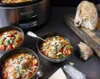 A slow cooker and bowls of soup are arranged on a dark surface, with bread and a grater nearby. Náhled obrázku produktu