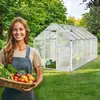 A woman holds a basket of fresh vegetables in front of a greenhouse. Produktbild-Vorschau