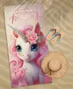 A beach scene with a unicorn towel, flip-flops, and a straw hat. Anteprima dell’immagine prodotto