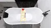 A top-down view of a modern, freestanding bathtub with a black headrest and a wooden tray holding bath accessories. Produktbild-Vorschau