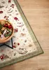 A close-up shot of a Christmas-themed rug with toys, placed on a wooden floor next to a table with Christmas decorations. Podgląd zdjęcia produktu