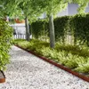 A garden path lined with white gravel and bordered by a rusty metal edge, leading past green bushes and trees. Náhled obrázku produktu