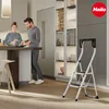 A couple is in a modern kitchen, with one person cooking and the other standing nearby. A step stool is positioned in the foreground. Podgląd zdjęcia produktu
