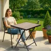 A woman sits on a patio next to a small folding table with a garden in the background. Anteprima dell’immagine prodotto
