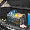 The image shows the interior of a car trunk with a foldable storage box filled with water bottles, cleaning supplies, and a paper bag. A blue cleaning bottle and two pink sponges are placed outside the box. Produktbild-Vorschau