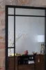 A mirror with a black frame reflecting a room with a sideboard, a lamp, and decorative items. Produktbild-Vorschau