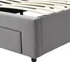 A close-up view of the corner of a gray upholstered bed frame, showing the wooden slats of the bed base and a drawer. Náhled obrázku produktu
