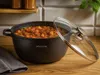 A pot of stew on a wooden table with a lid slightly ajar. Produktbild-Vorschau