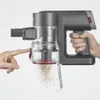 A person's hand is shown pressing a button on a cordless vacuum cleaner, causing dust to spill out of its transparent dustbin. Produktbild-Vorschau