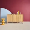 A wooden sideboard with decorative items on top, placed in a room with a maroon and light blue wall. Produktbild-Vorschau