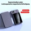 Two gray power banks are shown on a light gray surface. One is lying flat, and the other is standing upright, displaying its screen. Produktbild-Vorschau
