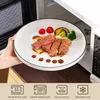A hand is placing a plate of food into a microwave. Voir les images du produit