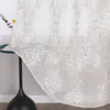 A sheer curtain with a floral pattern is draped over a small table next to a window. Produktbild-Vorschau