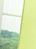 A close-up view of a green fabric panel, likely a curtain or blind, with a blurred background of trees and sky visible through a window. Produktbild-Vorschau
