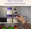 Baby bottles filled with milk are stacked inside a refrigerator, with a hand reaching for one. Voir les images du produit