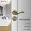 A close-up of a bronze door handle and lock set against a white and gray background, with a blurred interior scene on the left. Produktbild-Vorschau