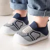 Paar blaue und weiße gestrickte Baby-Schlupfschuhe mit weißen Gummizehen, getragen an Babyfüßen mit umgeschlagenen Jeans Anteprima dell’immagine prodotto