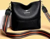 A black leather handbag with a colorful strap is displayed against a light beige background. Náhľad obrázku produktu
