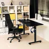 A black ergonomic office chair is positioned next to a black adjustable height desk in a home office setting with a white shelving unit in the background. Produktbild-Vorschau