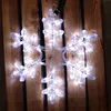 A lit snowflake decoration is placed on a wooden surface. Produktbild-Vorschau