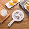 A close-up shot of a white mesh strainer with a handle, placed on a wooden table next to a glass of milk and some orange slices. Produktbild-Vorschau