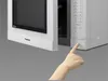 A hand is pressing a button on a microwave oven with its door open. Voir les images du produit
