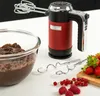 A red and black hand mixer is shown on a white surface next to a bowl of chocolate batter, beaters, and fresh berries. Produktbild-Vorschau