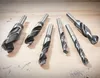 A collection of metal drill bits arranged on a wooden surface. Produktbild-Vorschau