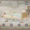 A wooden children's cot with bedding and a star-shaped pillow, set in a nursery-like environment with a play mat and wall art. Produktbild-Vorschau