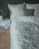 A neatly made bed with mint green striped bedding and a gray accent pillow, next to a small side table with a book and a glass of water. Náhled obrázku produktu
