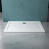 A white rectangular shower tray with a silver drain is placed on a concrete floor in front of a teal wall. Produktbild-Vorschau