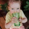 A young child drinks from a green glass. Produktbild-Vorschau