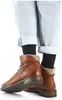 A pair of brown leather boots worn by a person with cuffed light blue jeans and black socks. Produktbild-Vorschau