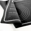 A black silicone baking mat with measurement markings and recipe suggestions is partially unrolled. Voir les images du produit