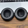 Two black ear pads with 'R' and 'L' markings are placed on a wooden surface in front of a laptop keyboard. Podgląd zdjęcia produktu
