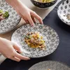 Hands are arranging plates with food on a table with a dark blue tablecloth. Náhled obrázku produktu