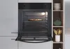 An open oven with a pizza inside, next to a shelf with kitchenware. Náhľad obrázku produktu