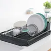 A dark gray dish rack filled with clean dishes and utensils on a white countertop. Podgląd zdjęcia produktu